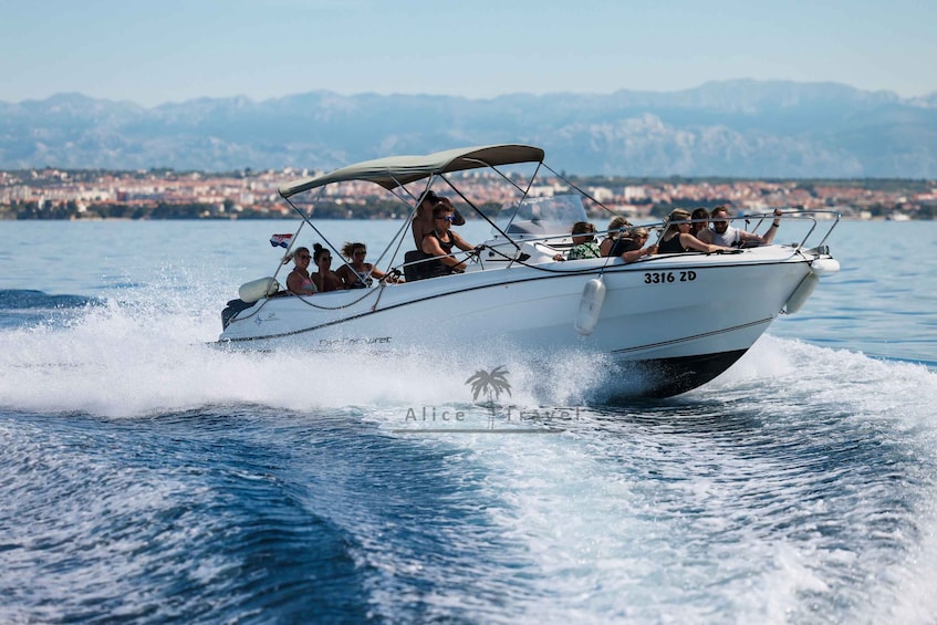 A white speedboat with the number 3316 ZD on the back, moving swiftly through the water with passengers on board. 1