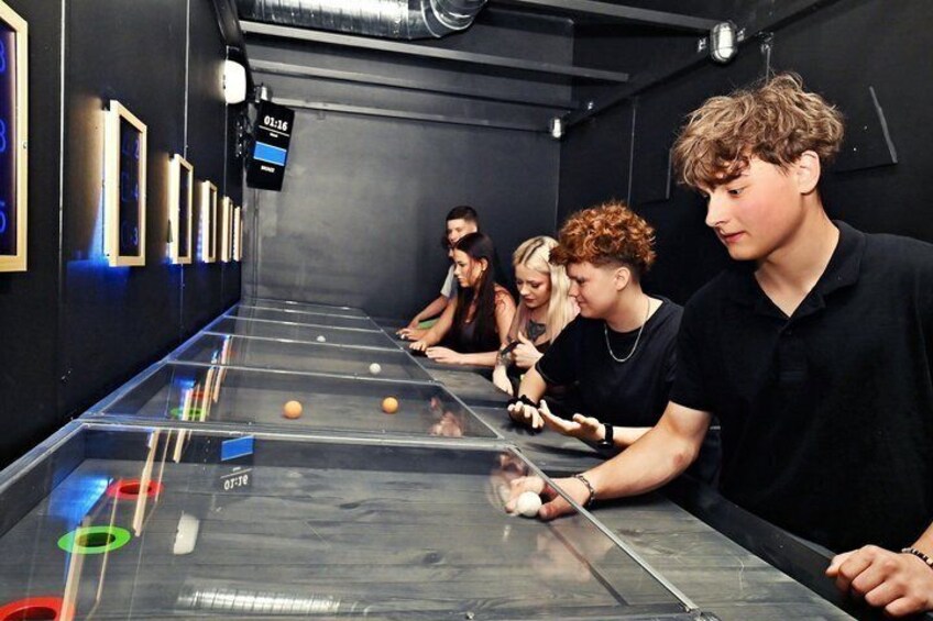 A billiards table with players, a digital timer, and framed pictures on the wall. 3