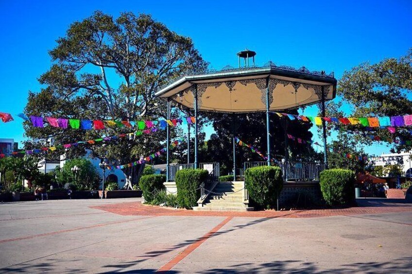 A gazebo with colorful flags, surrounded by greenery and a clear blue sky. 3