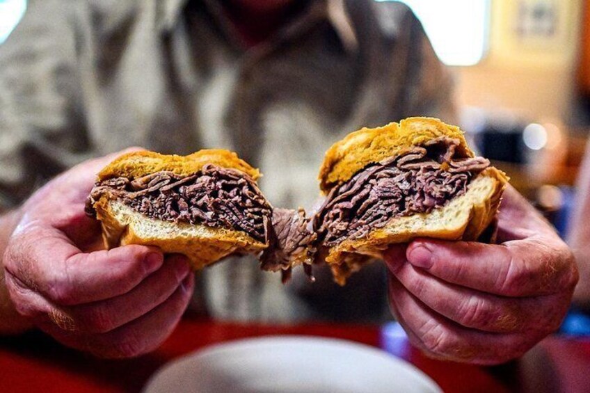 A person holding a sandwich with a visible filling of meat and sauce. 1