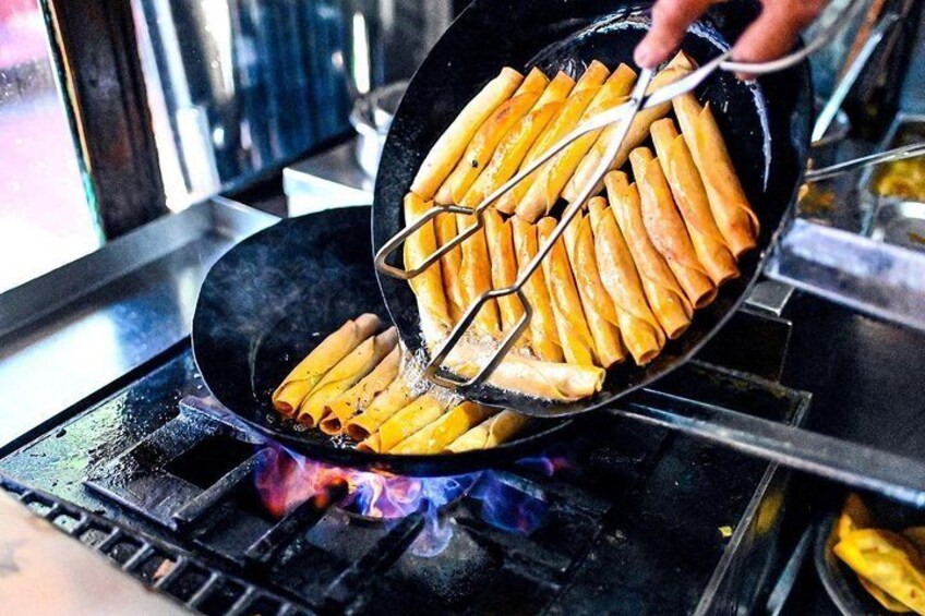 A person cooking spring rolls in a pan on a stove. 4