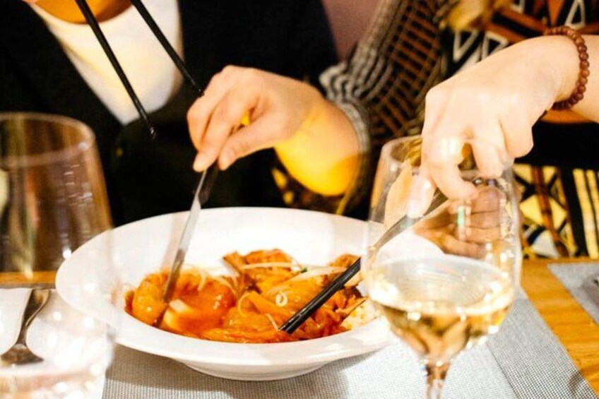 A person eating pasta with a fork and knife, a glass of white wine, and a glass of water on a table. 3
