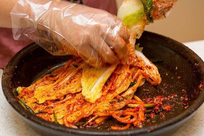 A person preparing a dish with sliced vegetables and a red sauce in a black pan. 5