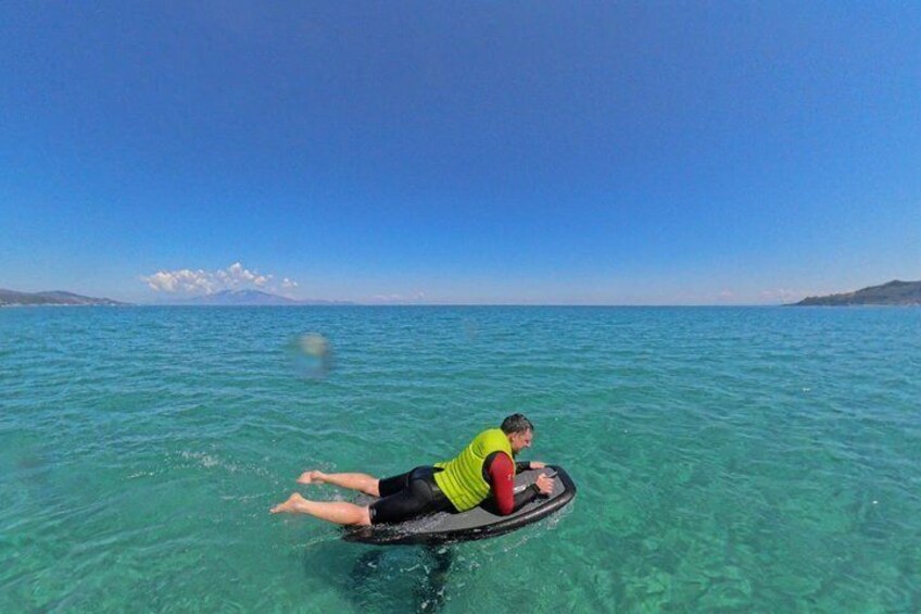 A person lying on a board in clear blue water with a distant mountain and sky. 4