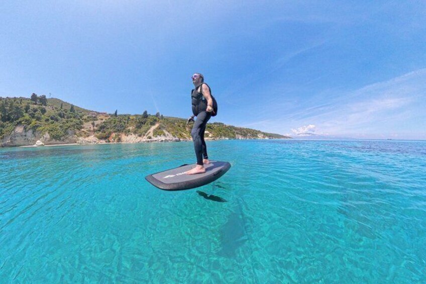 A person surfing on a clear blue sea with a hilly coastline in the background. 5