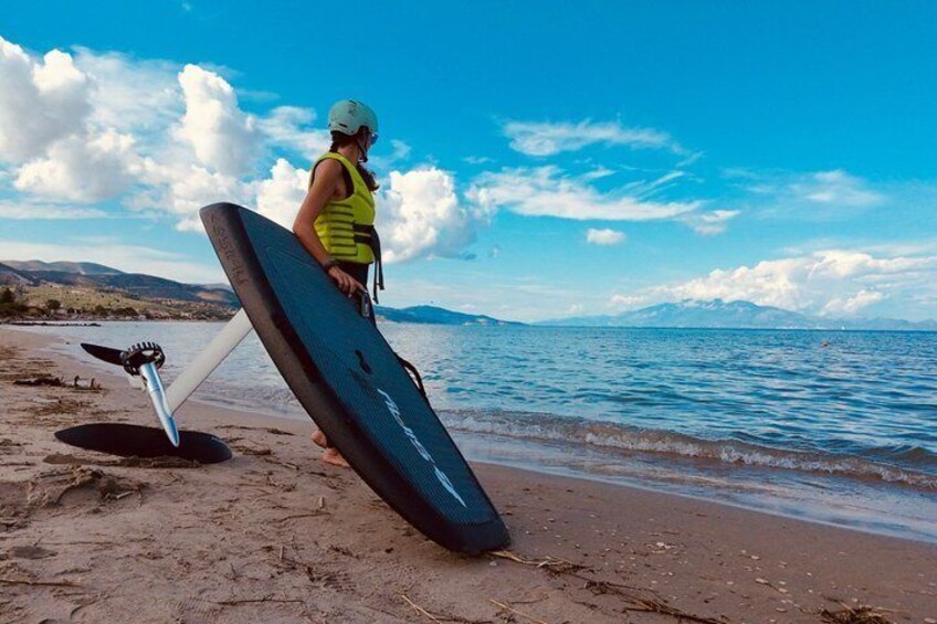 A person with a paddleboard on a sandy beach, water in the background, and mountains in the distance. 2