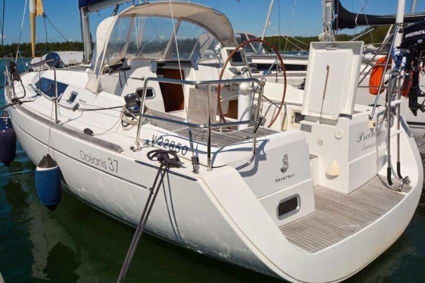 A white sailboat named 'Oceanis 37' docked at a marina with a covered deck area and a small cabin. 2