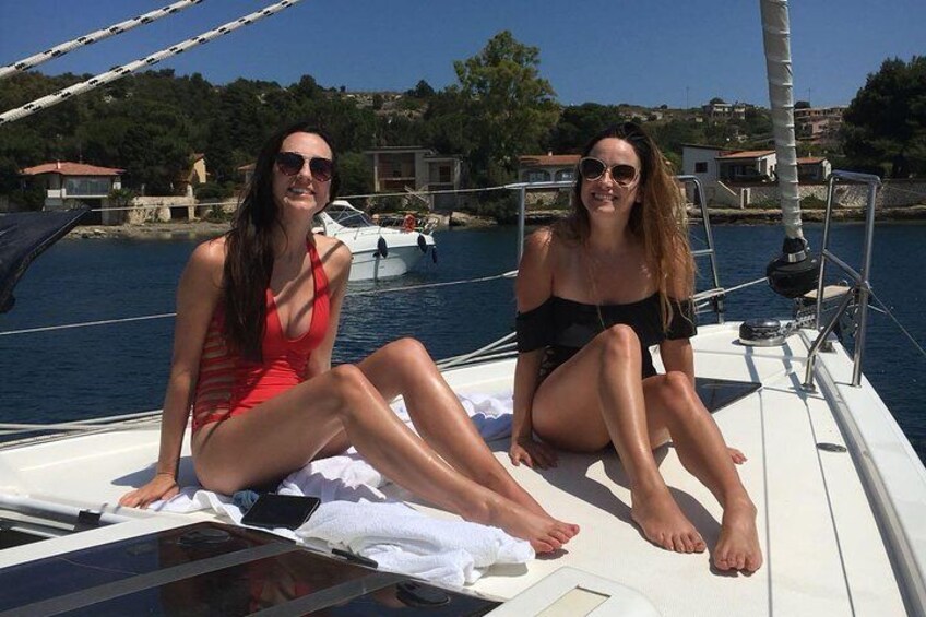 Two people on a sailboat with a marina and buildings in the background. 1