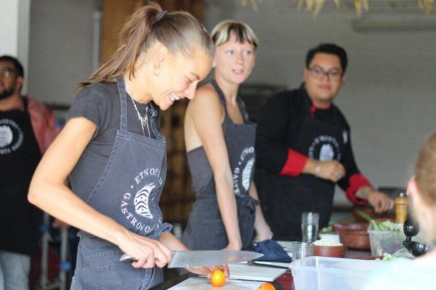 A person cutting an orange at a table with other people in aprons. 2