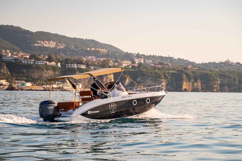 A speedboat named 'LABO' with a Yamaha engine, sailing on calm waters with a coastal town and cliffs in the background. 1