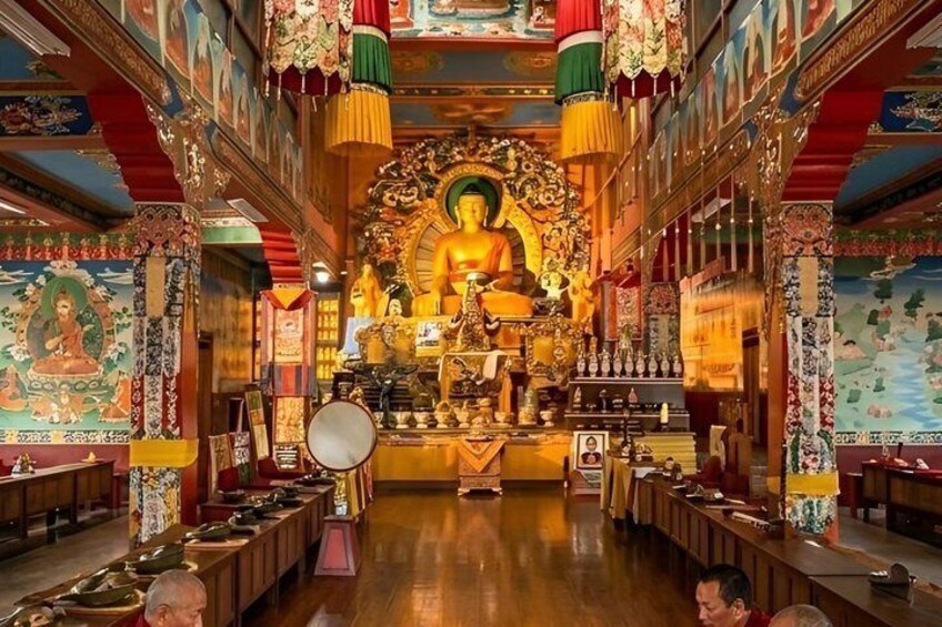 A temple interior with a large Buddha statue, prayer wheels, and intricate wall paintings. 1