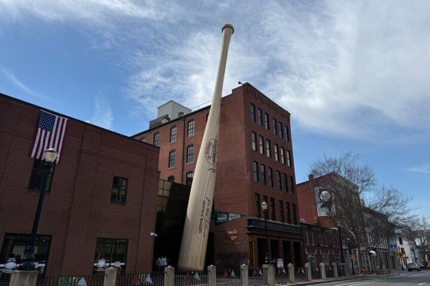 A tall wooden baseball bat leaning against a brick building with an American flag. 5