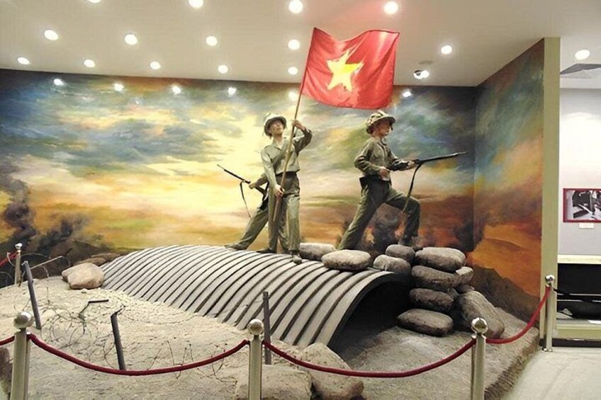 A museum exhibit with two soldiers holding flags, a rocky landscape, and a sunset mural in the background. 5