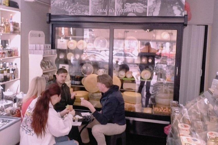 A group of people at a cheese shop with a variety of cheeses on display. 4