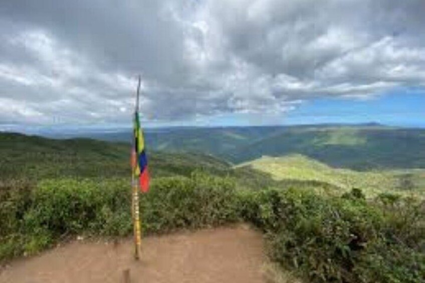 A flagpole on a hilltop with a view of a valley and distant mountains. 5