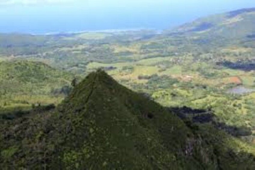A green hill with a small mound in the foreground and a valley with scattered buildings in the background. 2