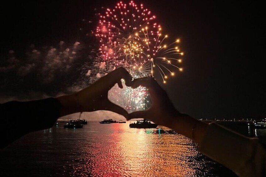 Hands forming a heart shape with fireworks in the background. 1