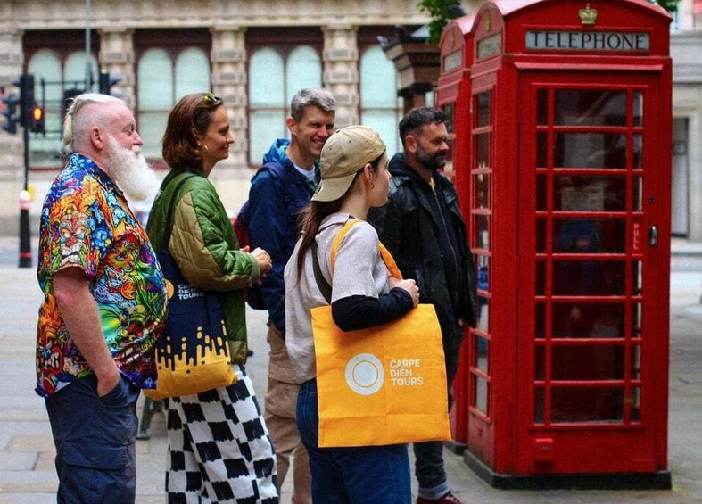 A group of people standing in front of a red telephone booth. 5