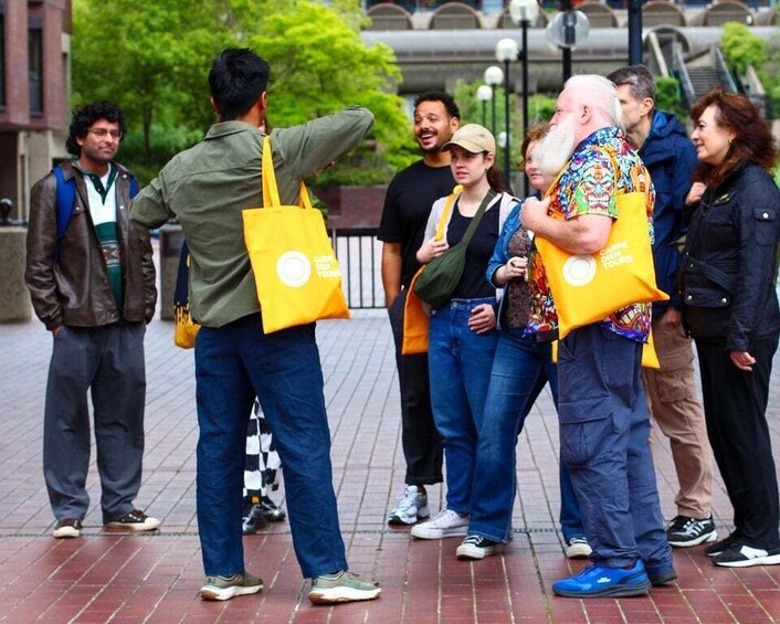 A group of people standing on a brick pavement, some holding yellow bags. 3