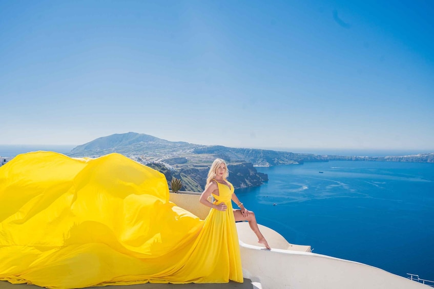 A person in a yellow dress on a cliff overlooking a coastal landscape with a mountain in the distance. 4