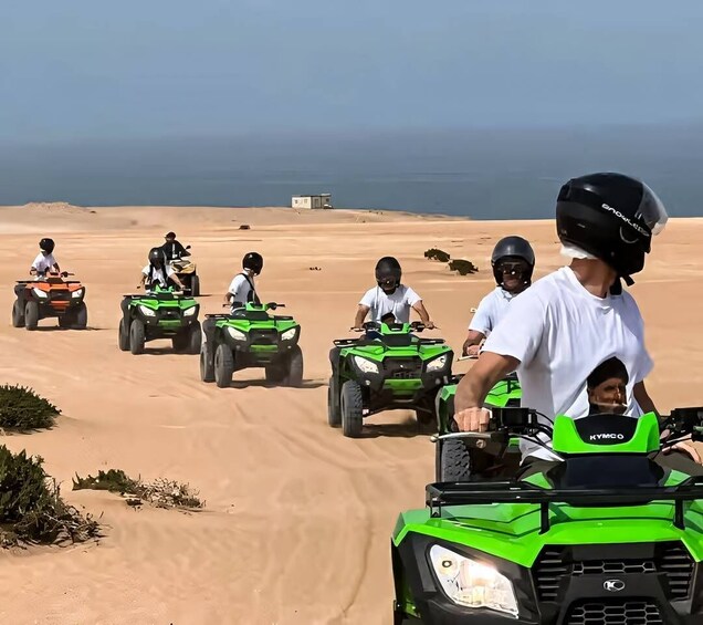 People riding ATVs on a sandy terrain with a clear sky and a building in the distance. 1