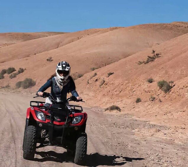 A person riding a red ATV on a dirt road in a desert landscape. 2