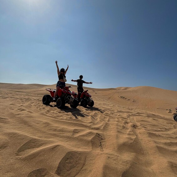 Two people on red quad bikes in a desert with sand dunes. 4