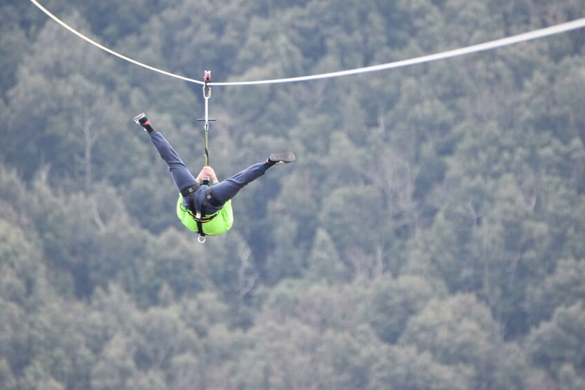 A person bungee jumping with a harness and safety gear, suspended by a bungee cord above a forested landscape. 1