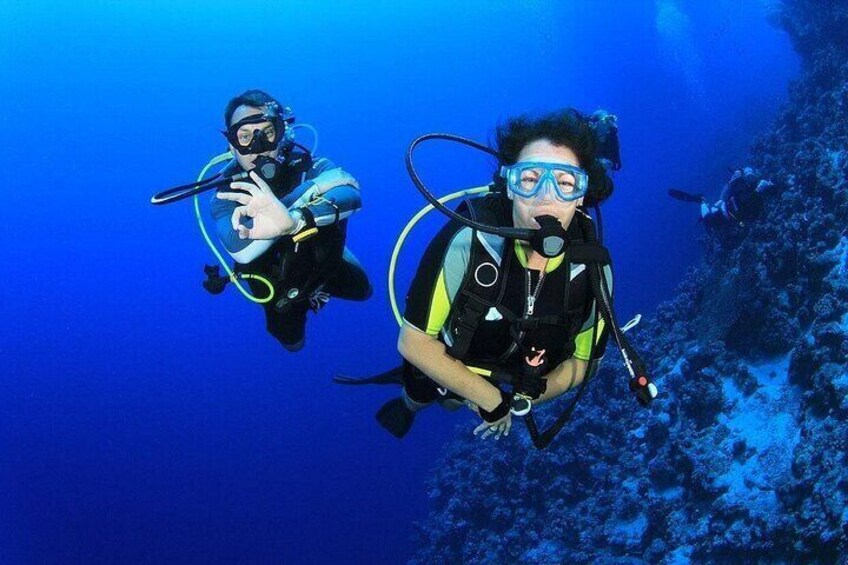 Two scuba divers underwater with coral formations in the background. 1