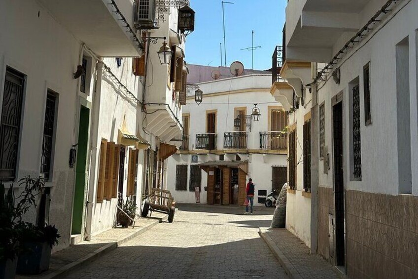 A narrow cobblestone street flanked by white buildings with balconies and wooden shutters. 4
