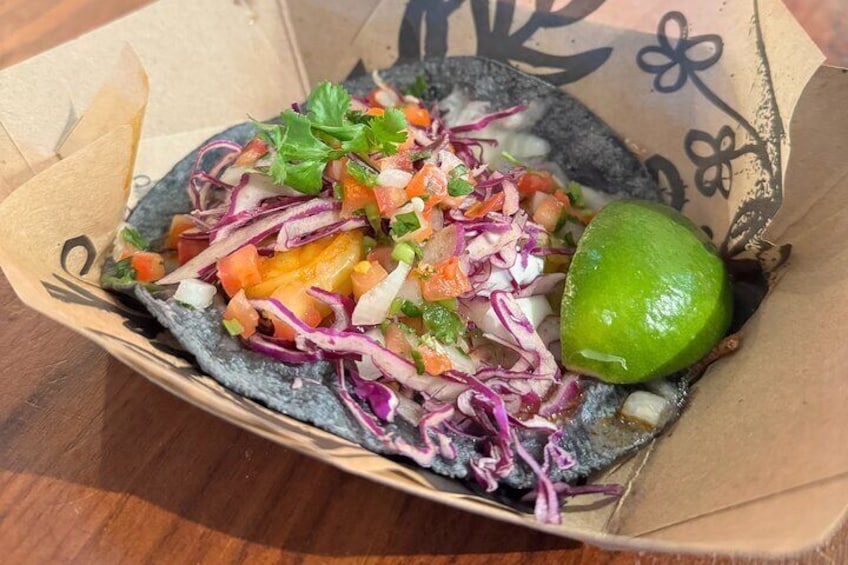 A taco with toppings and a lime wedge in a paper container. 1