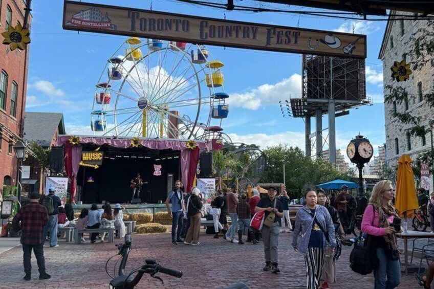 A Ferris wheel, a stage with a band, and a crowd at the Toronto Country Fest. 3