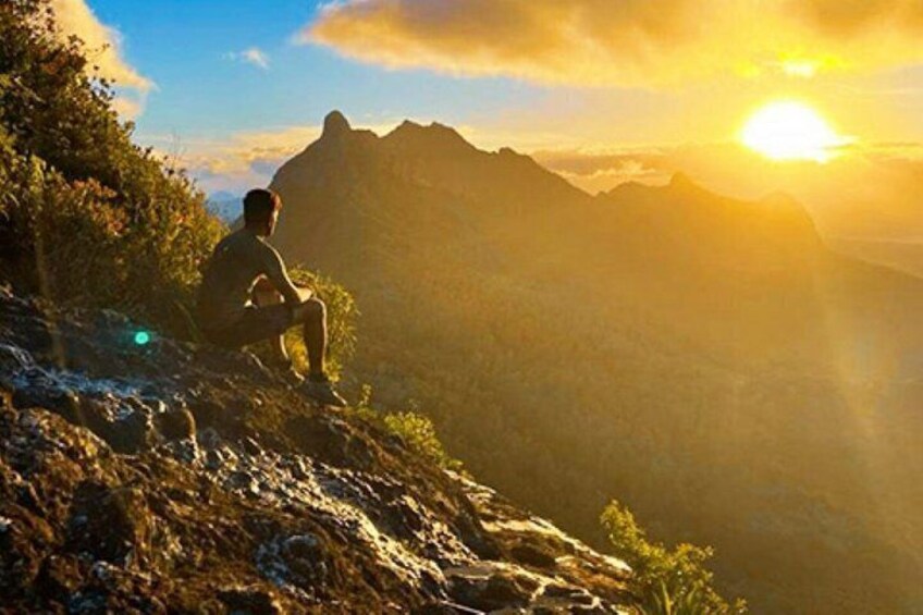A person sitting on a rocky outcrop overlooking a mountainous landscape during sunset. 2
