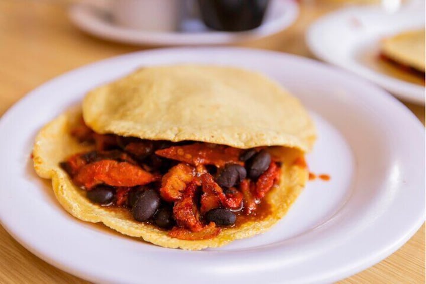 A plate with a food item that appears to be a stuffed pastry, possibly a type of empanada, filled with a red sauce and black beans. 2