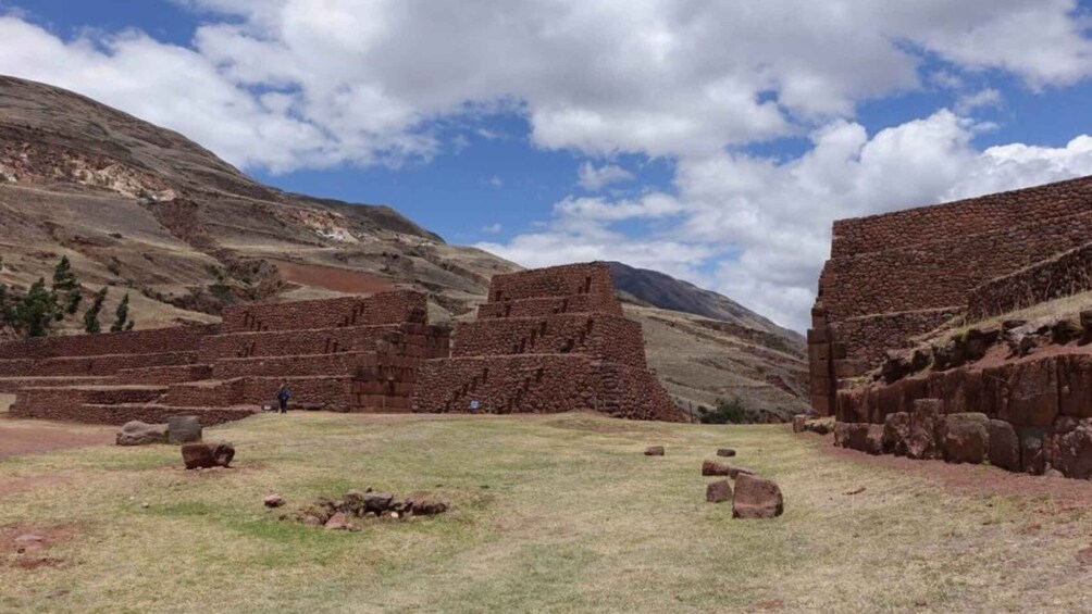 Ancient brick ruins in a grassy field with mountains in the background. 5