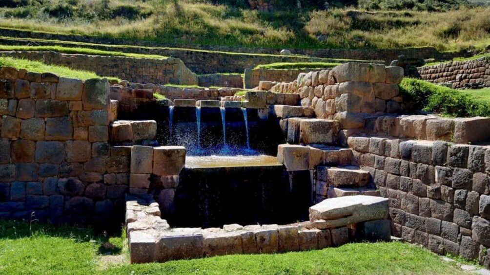 A stone-built water feature with cascading water, surrounded by terraced grassy areas. 1