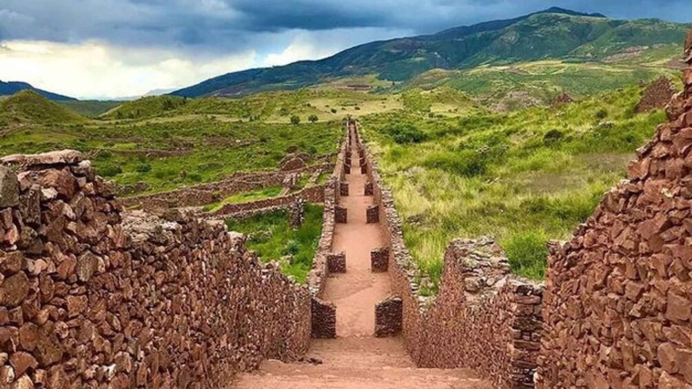 A stone pathway leading through a rural landscape with terraced fields and mountains in the background. 4