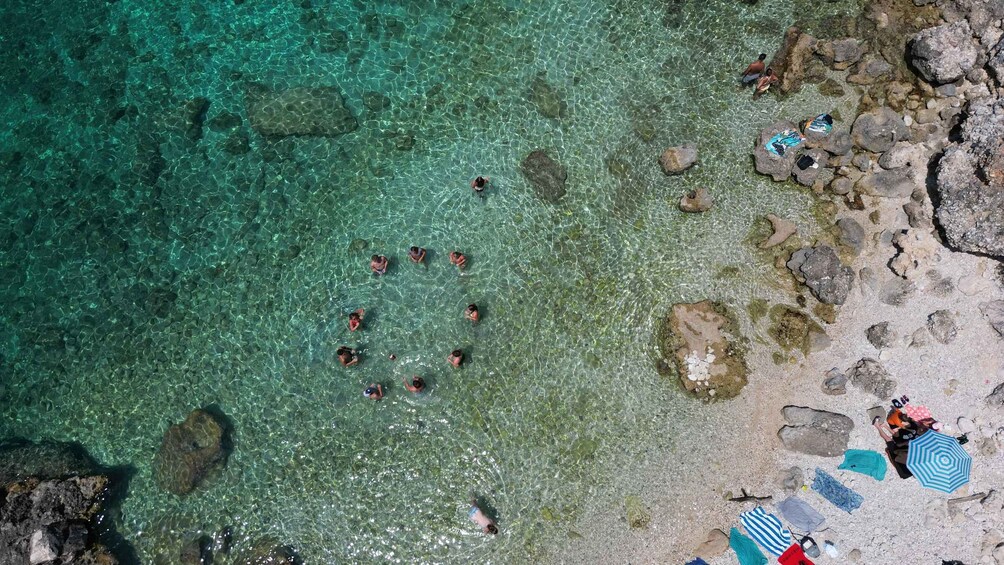 A group of people swimming in clear turquoise water, surrounded by rocks and pebbles. 3