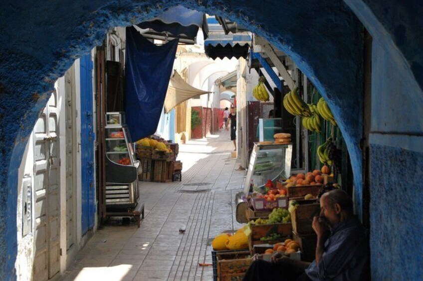 A narrow street with fruit stalls and a blue archway. 2