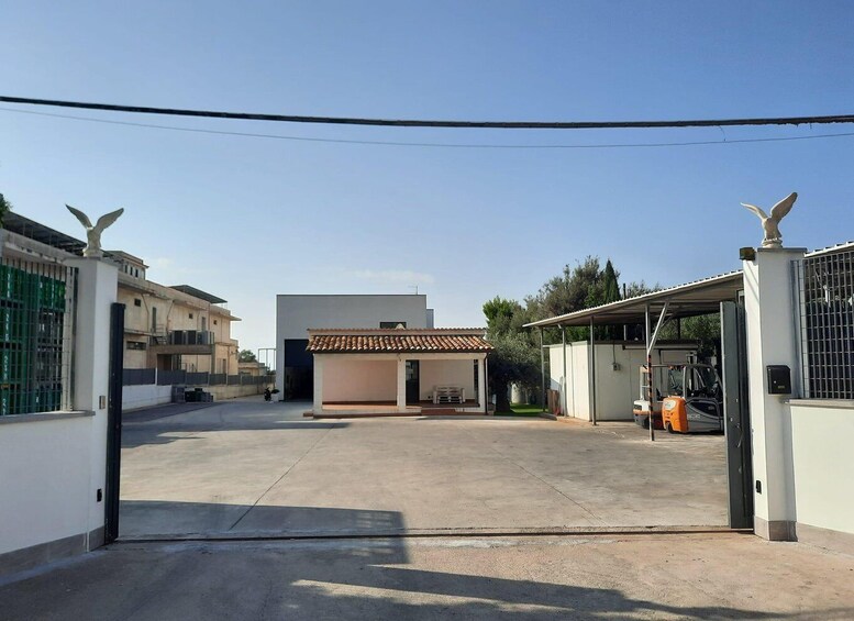 A gated parking area with a small building, a modern house, and a parked forklift. 1
