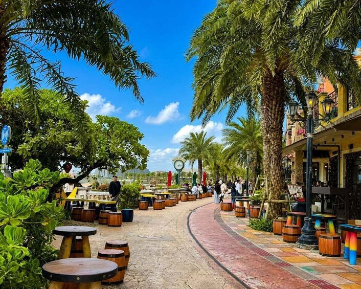 A sunny outdoor café with wooden tables and chairs, surrounded by palm trees and greenery. 1