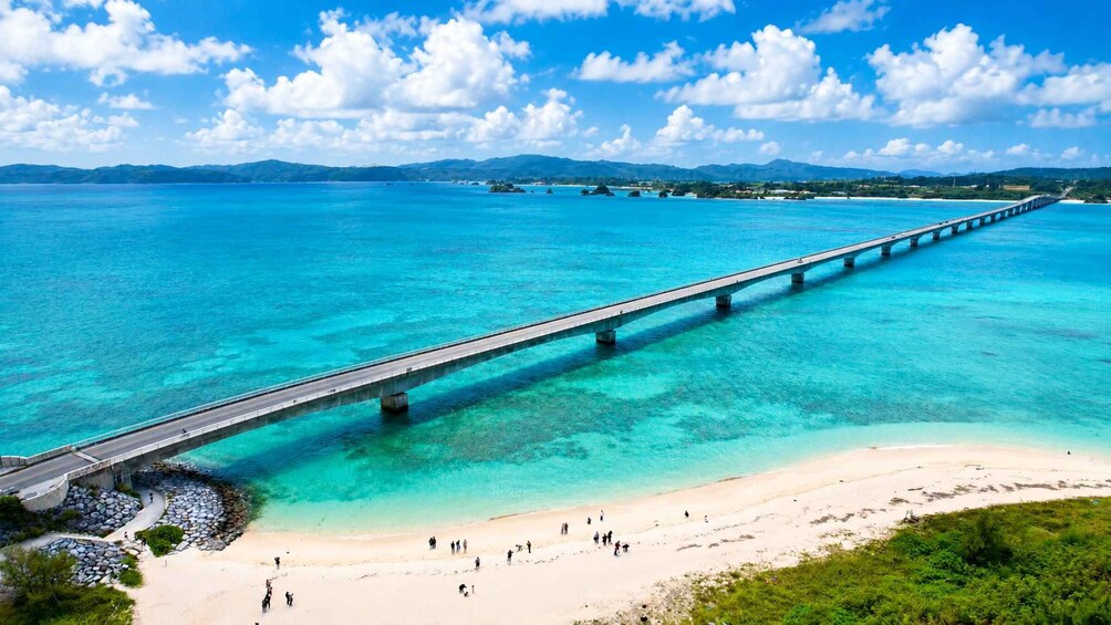 A long bridge over turquoise waters, a sandy beach, and distant mountains. 1