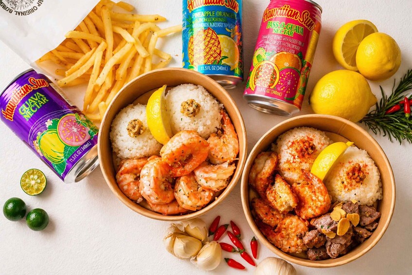 Two bowls of shrimp and rice with lemon slices, surrounded by French fries, canned drinks, and lemons. 2