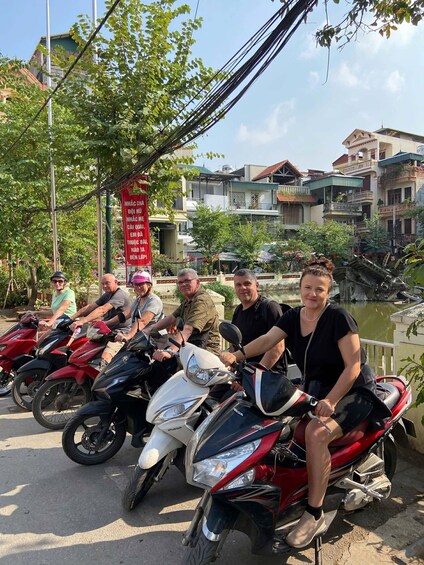 A group of people on scooters parked by a canal with buildings in the background. 4