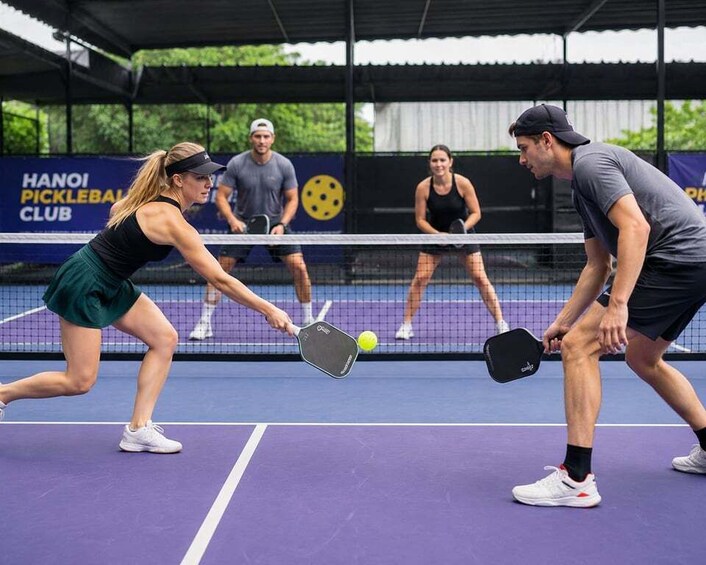 A tennis match in progress on an outdoor court with a 'HANOI PICKLEBALL CLUB' sign in the background. 2