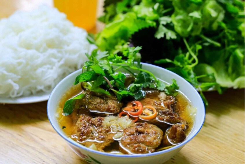 A bowl of soup with meatballs, garnished with herbs, and a plate of white rice in the background. 3
