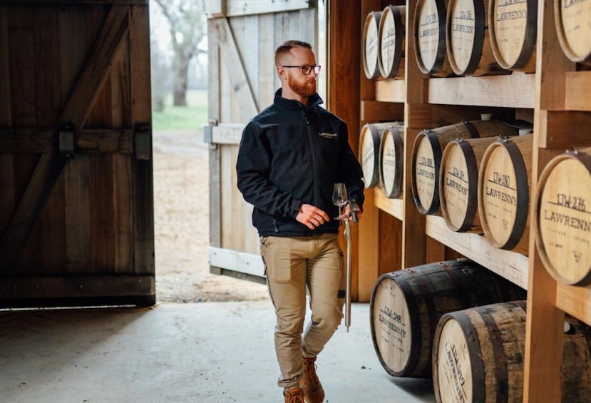 A person standing in a warehouse with wooden barrels labeled 'LAWRENCE' on shelves. 1