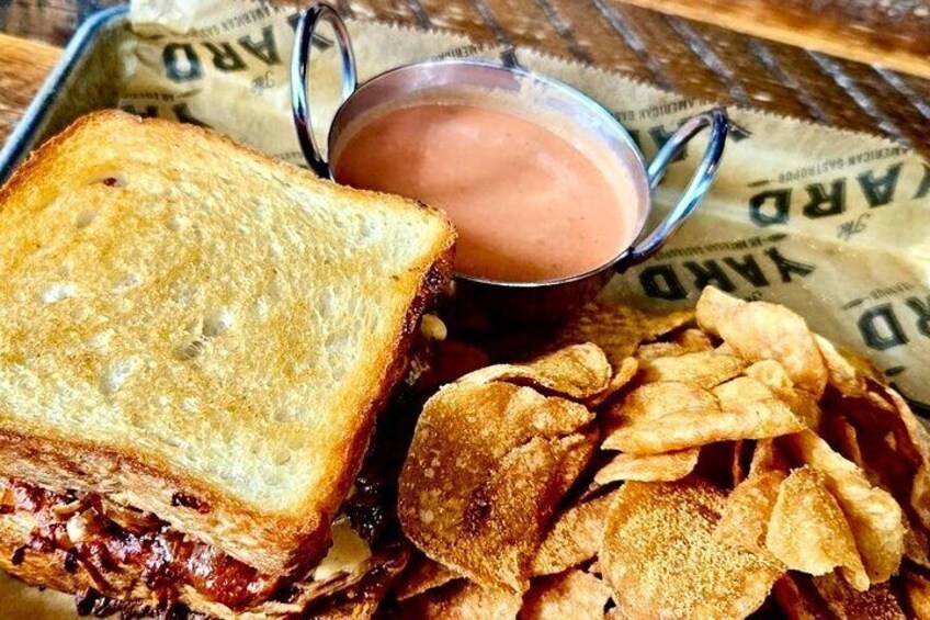 A grilled sandwich, a bowl of sauce, and a pile of chips. 1