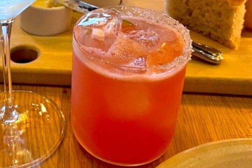 A glass of pink beverage with a salted rim, a glass of water, and a slice of bread on a wooden table. 5