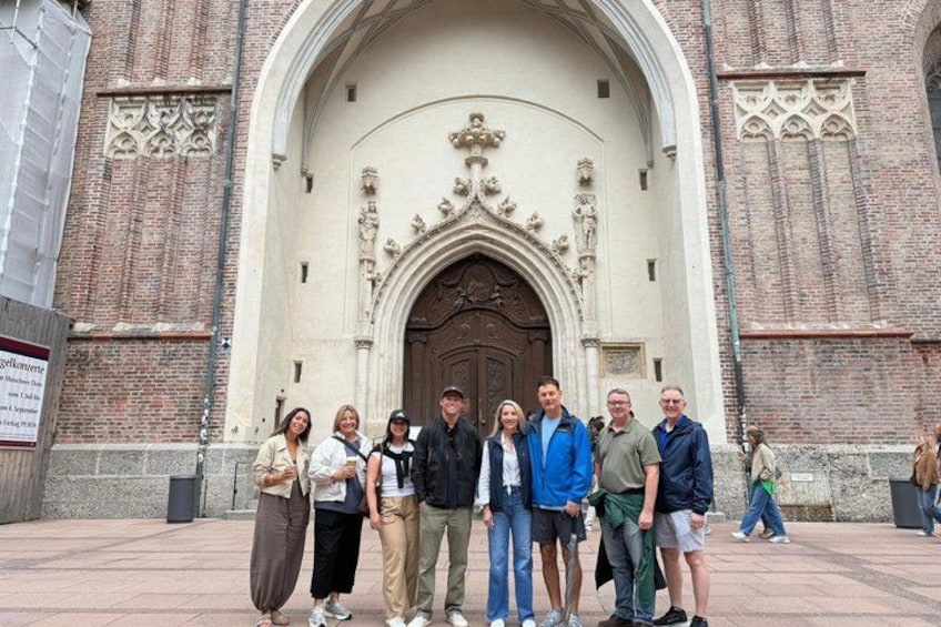 A group of people standing in front of a historic building with a large arched doorway and intricate stone carvings. 2